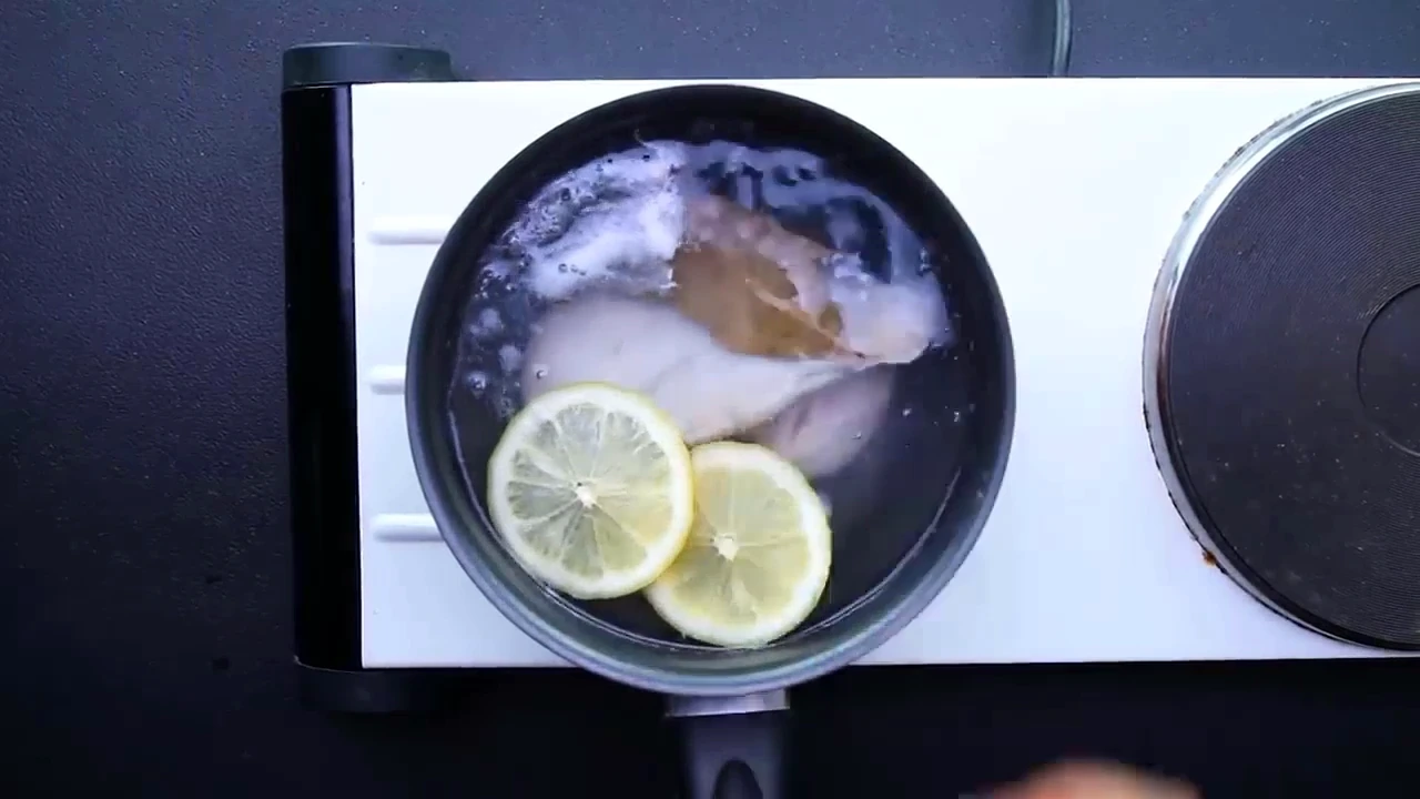 Chicken breast poaching with lemon slices and bay leaves.