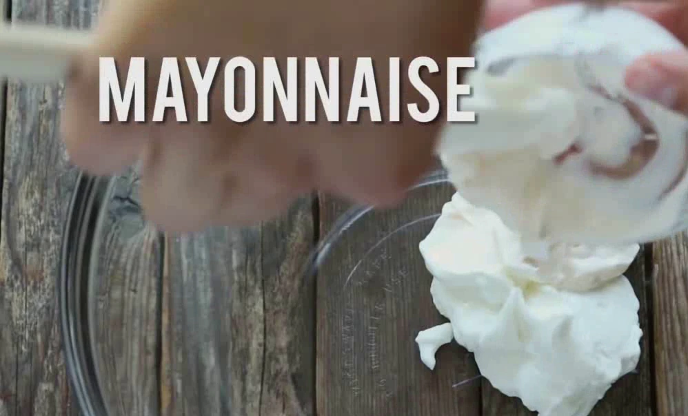 Adding Greek yogurt and mayonnaise to a bowl for chicken salad stuffed avocados.