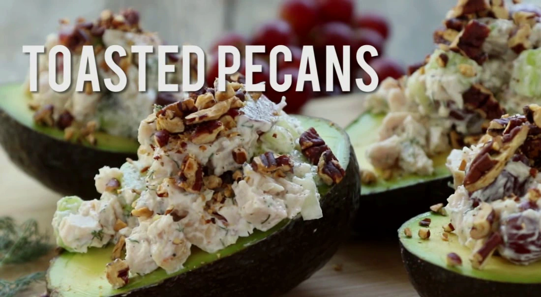 Topping chicken salad stuffed avocados with toasted pecans.