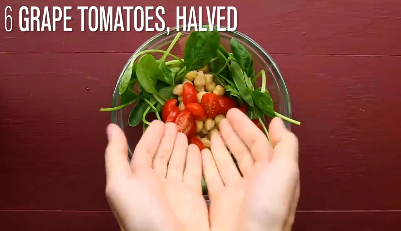 Adding halved tomatoes to chickpea spinach salad