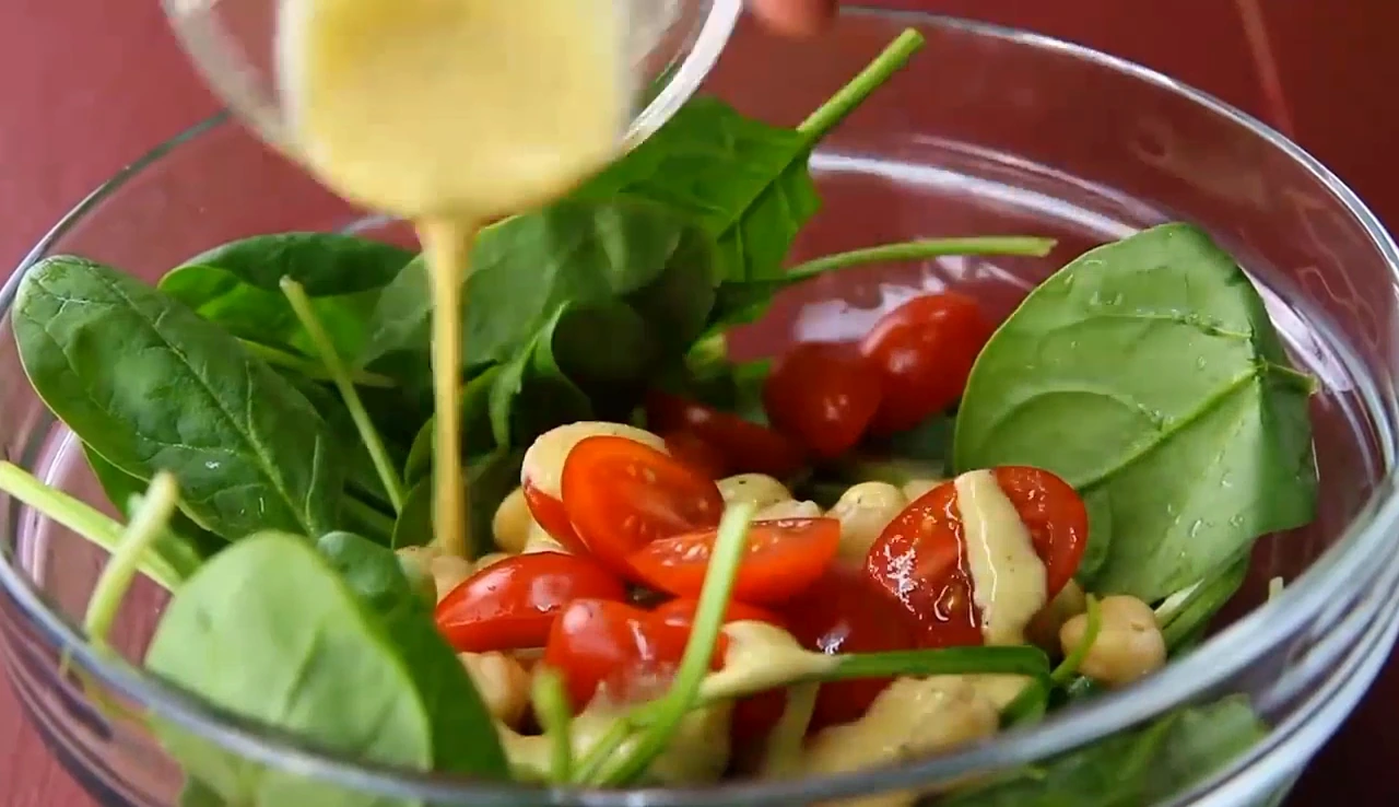 Pouring dressing over chickpea spinach salad