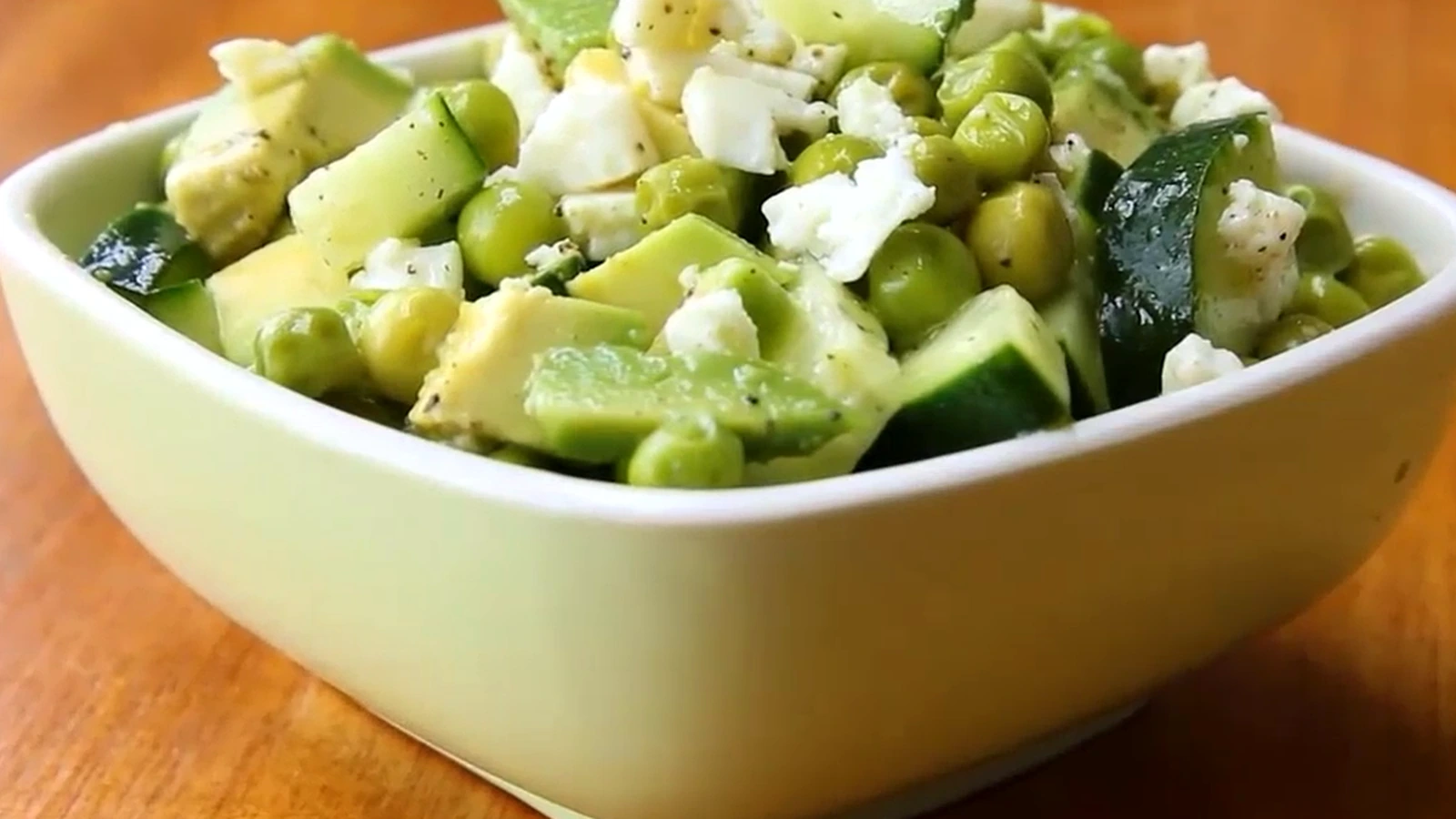 Cucumber avocado salad with peas and feta in a pale green bowl.