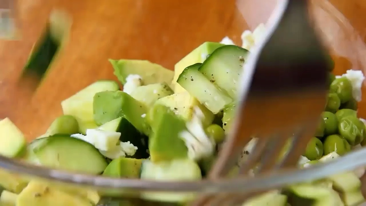 Tossing cucumber avocado salad until coated.