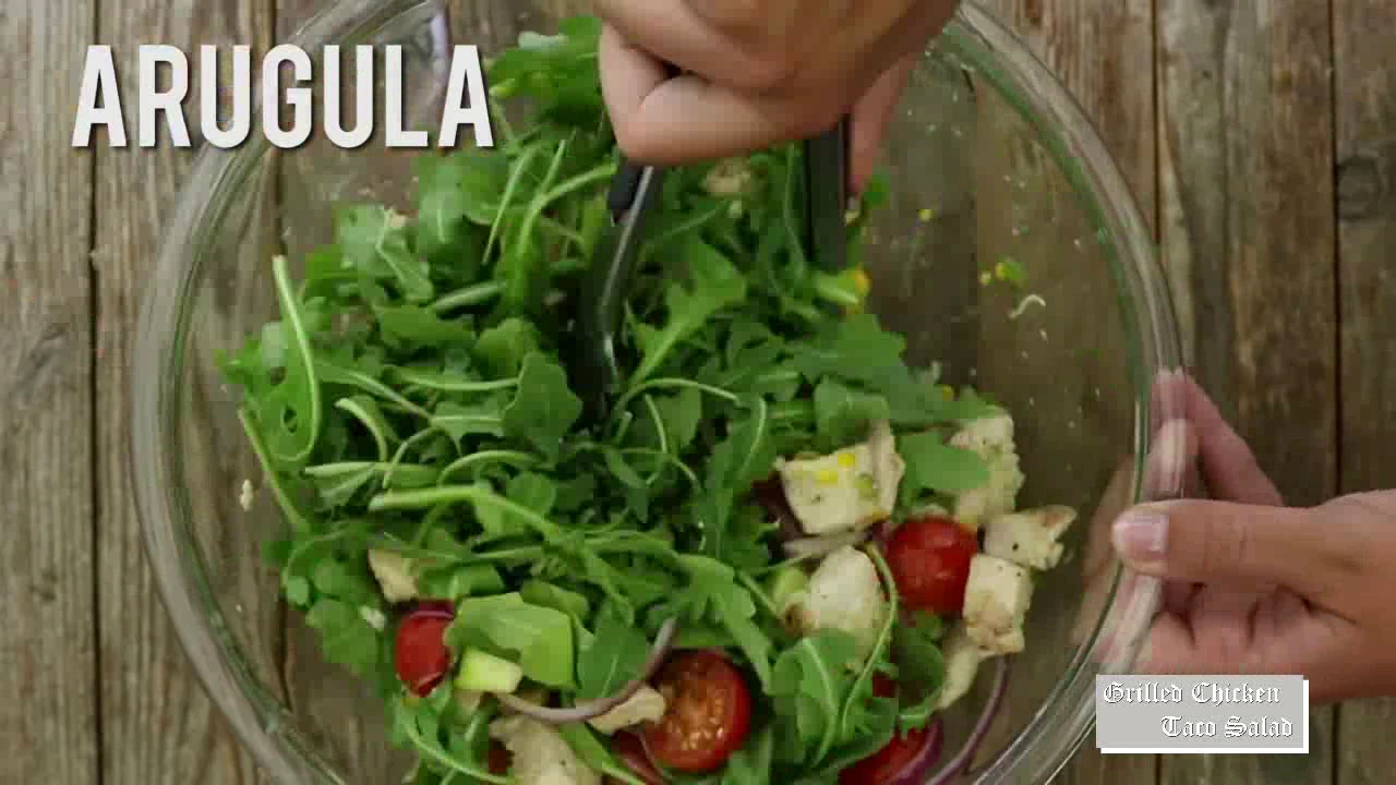 Adding arugula to grilled chicken taco salad.