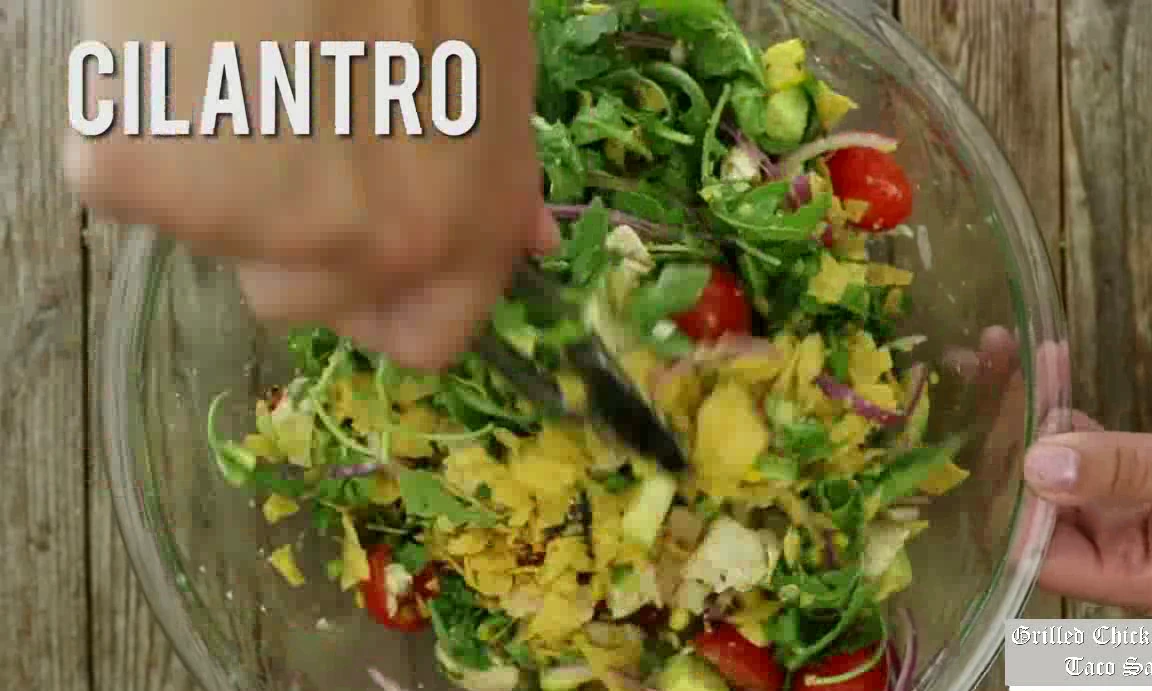 Adding tortilla chips and cilantro to grilled chicken taco salad.