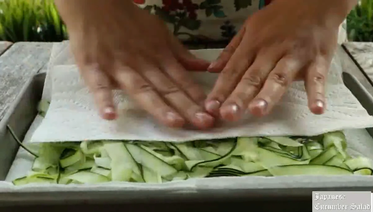 Pressing cucumber ribbons dry with paper towels.