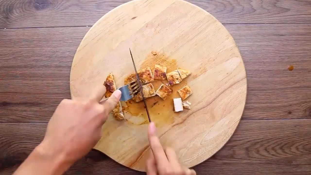Cooked chicken being sliced for meal prep salad