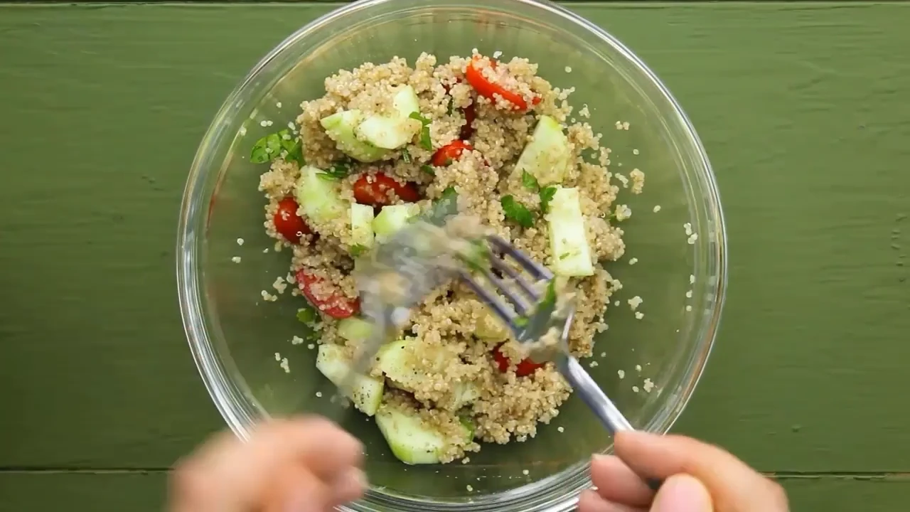 Tossing quinoa salad with avocado in a bowl.