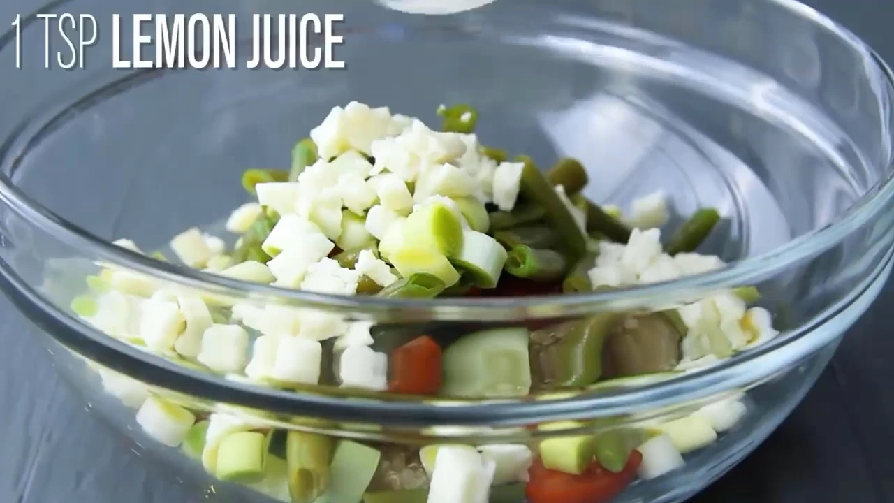 Drizzling lemon juice into quinoa salad with feta.