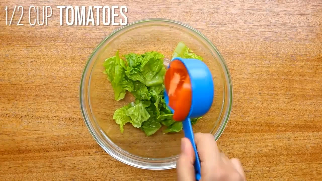 Adding tomatoes to lettuce for roasted chicken salad.