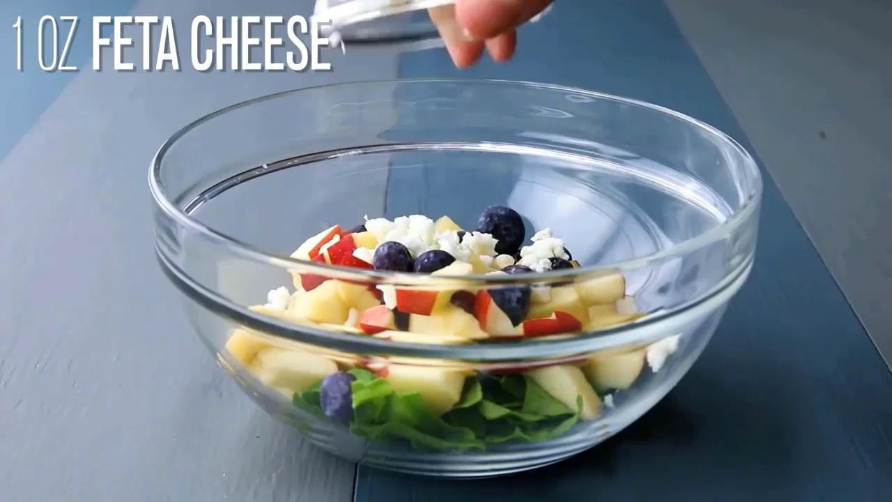 Spinach, apple, blueberries, feta, and walnuts being added to a bowl