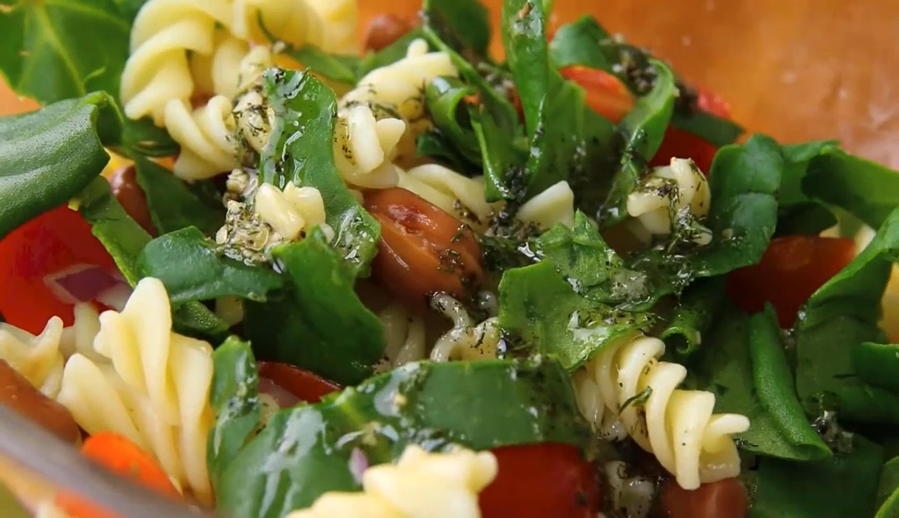 Pouring dressing over spinach pasta salad