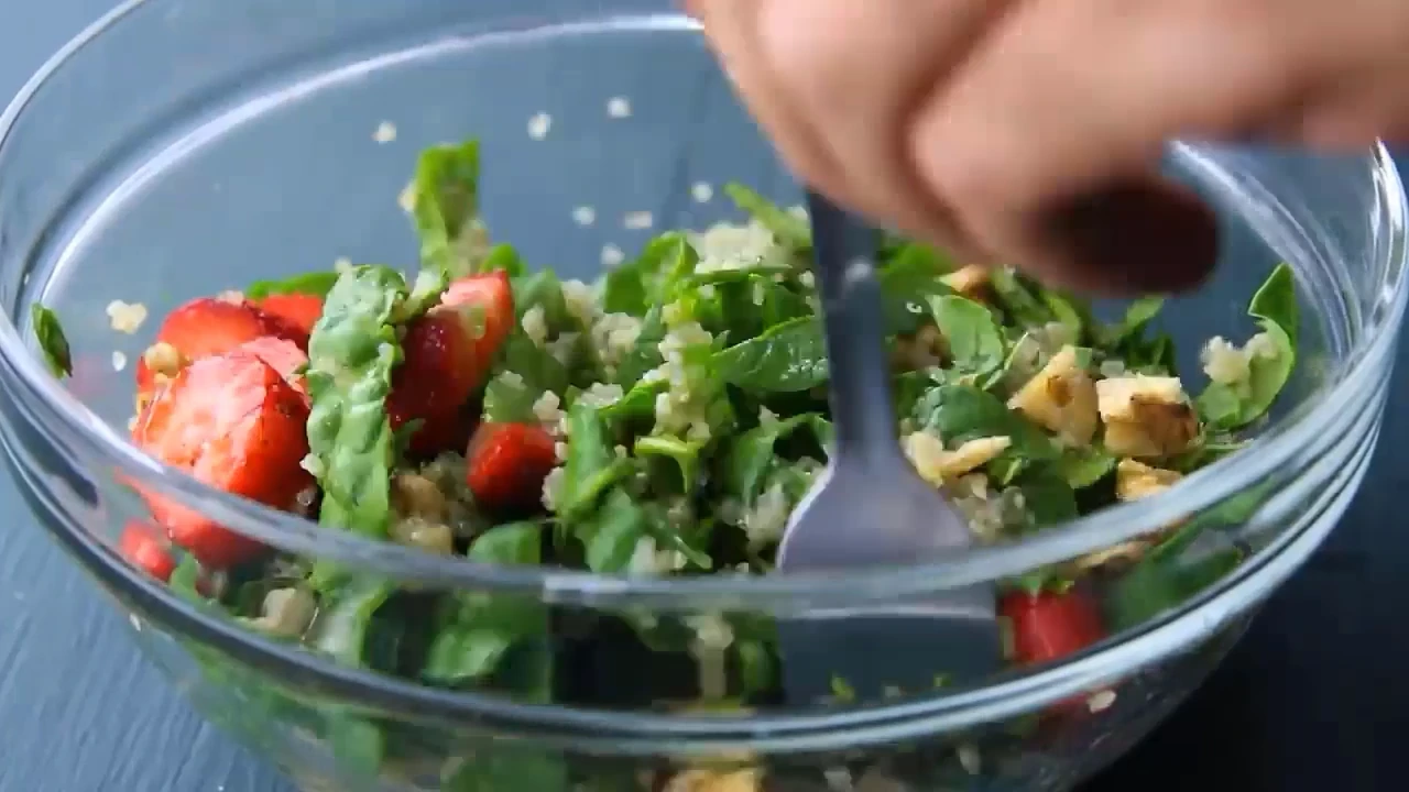 Tossing strawberry spinach quinoa salad in a bowl.