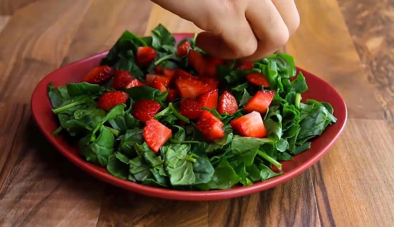 Adding strawberries over chopped spinach