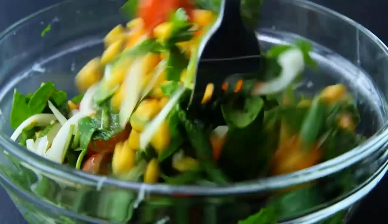 Pouring dressing over spinach and corn salad