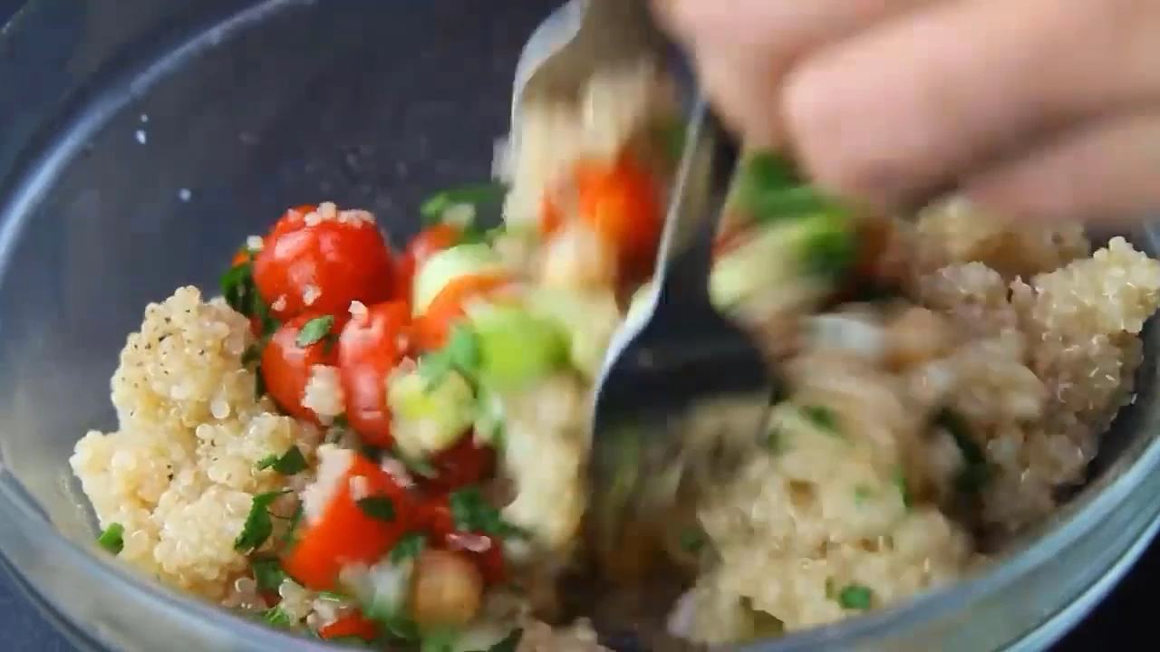 Tossing tomato quinoa salad in a bowl.
