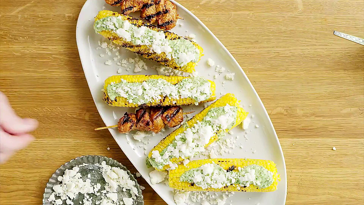 Pork skewers arranged with dressed grilled corn