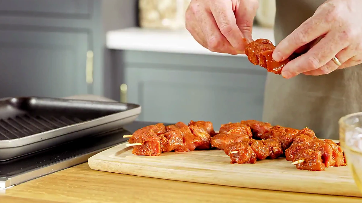 Marinated pork being threaded onto skewers