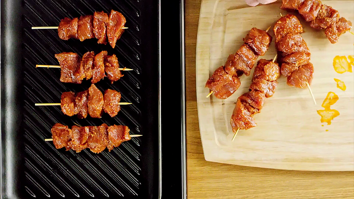 Raw pork skewers arranged beside the grill pan
