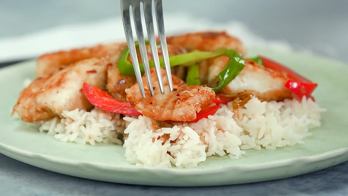 Close view of crispy fish with peppers over rice
