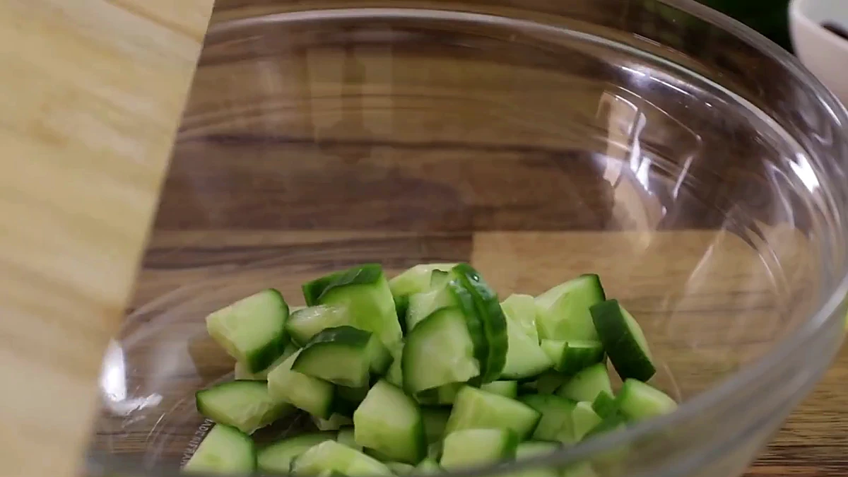 Chopped cucumber added to a glass mixing bowl