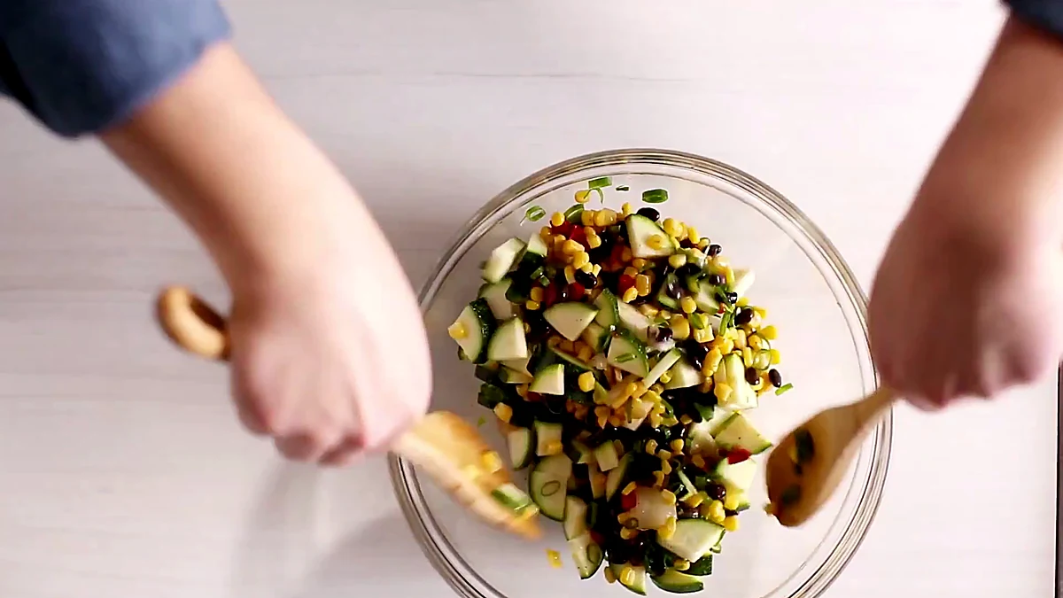 Corn and zucchini salad being tossed in a glass bowl