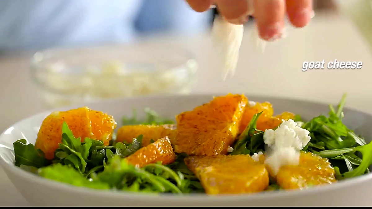 Goat cheese sprinkled over orange arugula salad