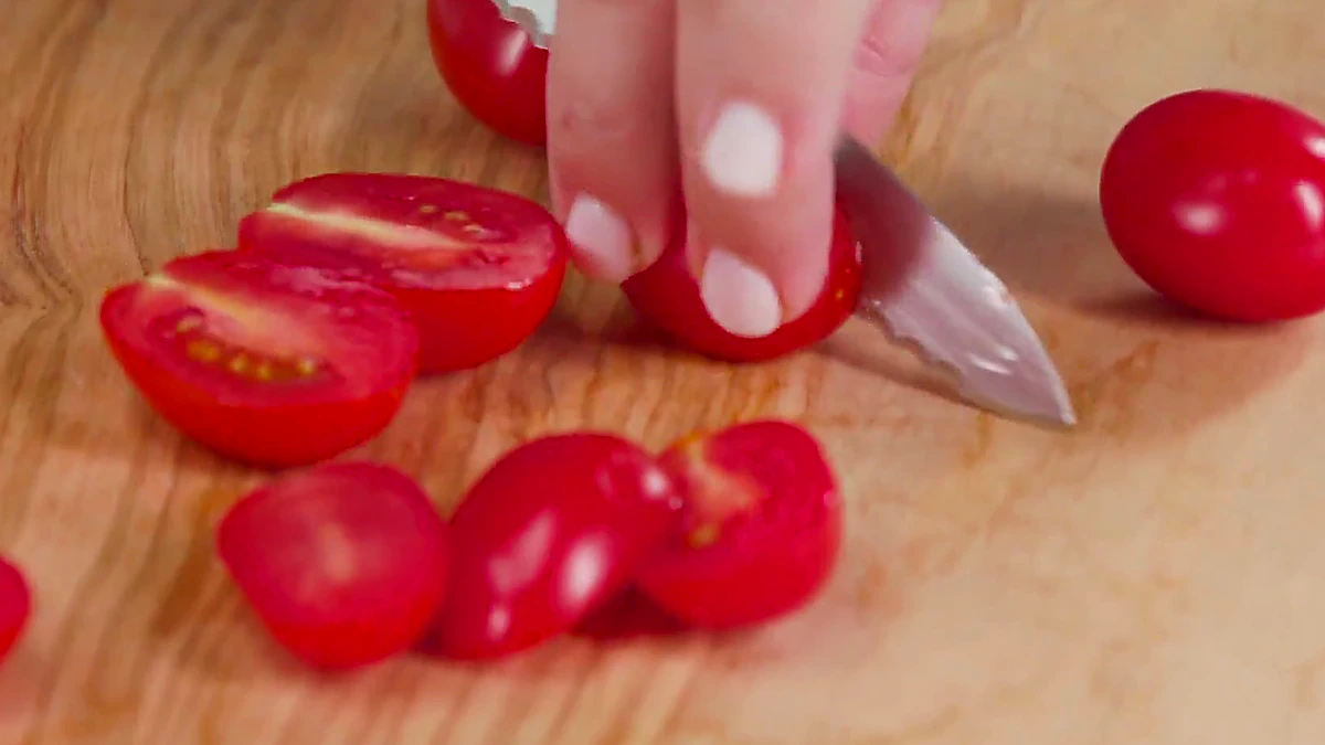 Grape tomatoes being halved on a cutting board