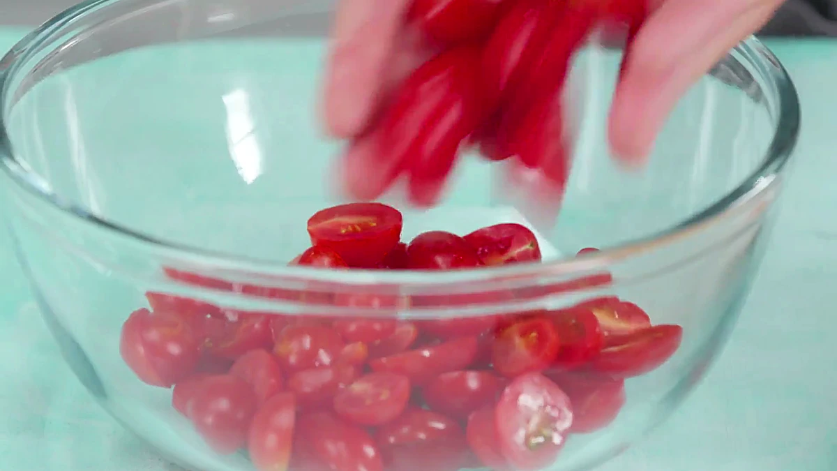 Halved grape tomatoes being moved into a mixing bowl