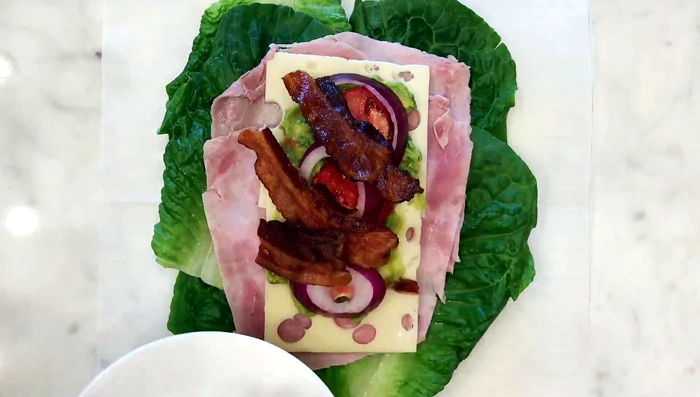 Cooked bacon strips added to a lettuce wrap sandwich