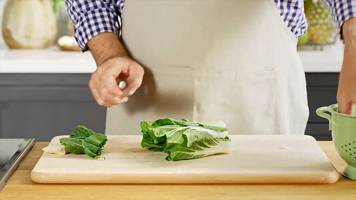 Baby bok choy halved on a cutting board next to a chef knife