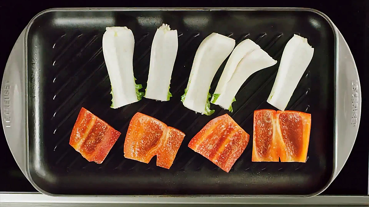 Bok choy halves and red pepper chunks getting grill marks on a grill pan