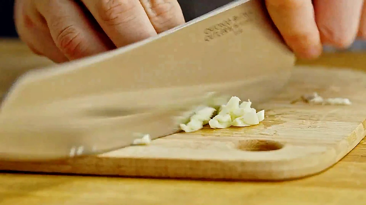 Garlic being minced on a cutting board for the warm salad