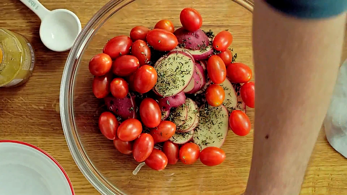 Sliced potatoes and grape tomatoes tossed with thyme in a glass bowl