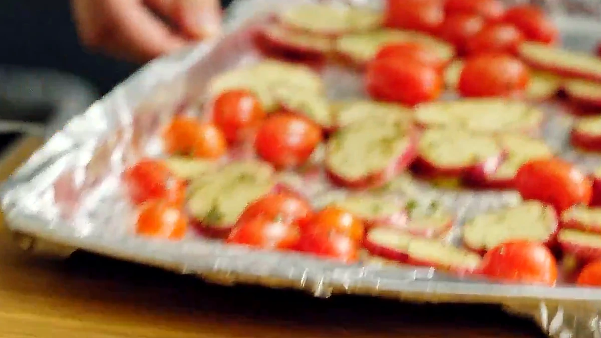 Potatoes and tomatoes spread out on a foil lined sheet pan