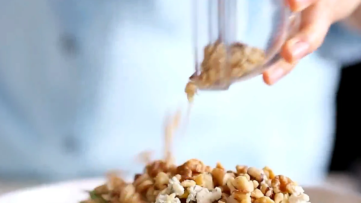 Chopped walnuts being added to the pear and arugula salad