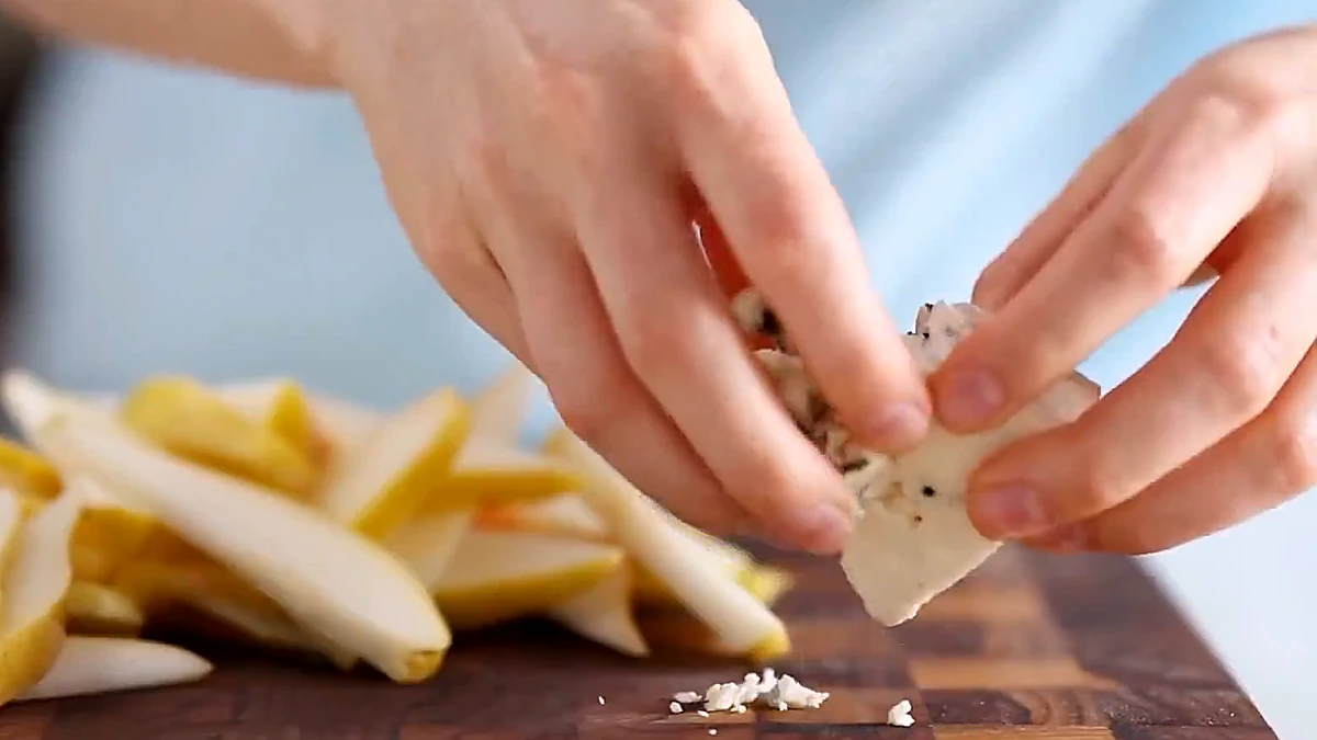 Blue cheese being crumbled over sliced pears