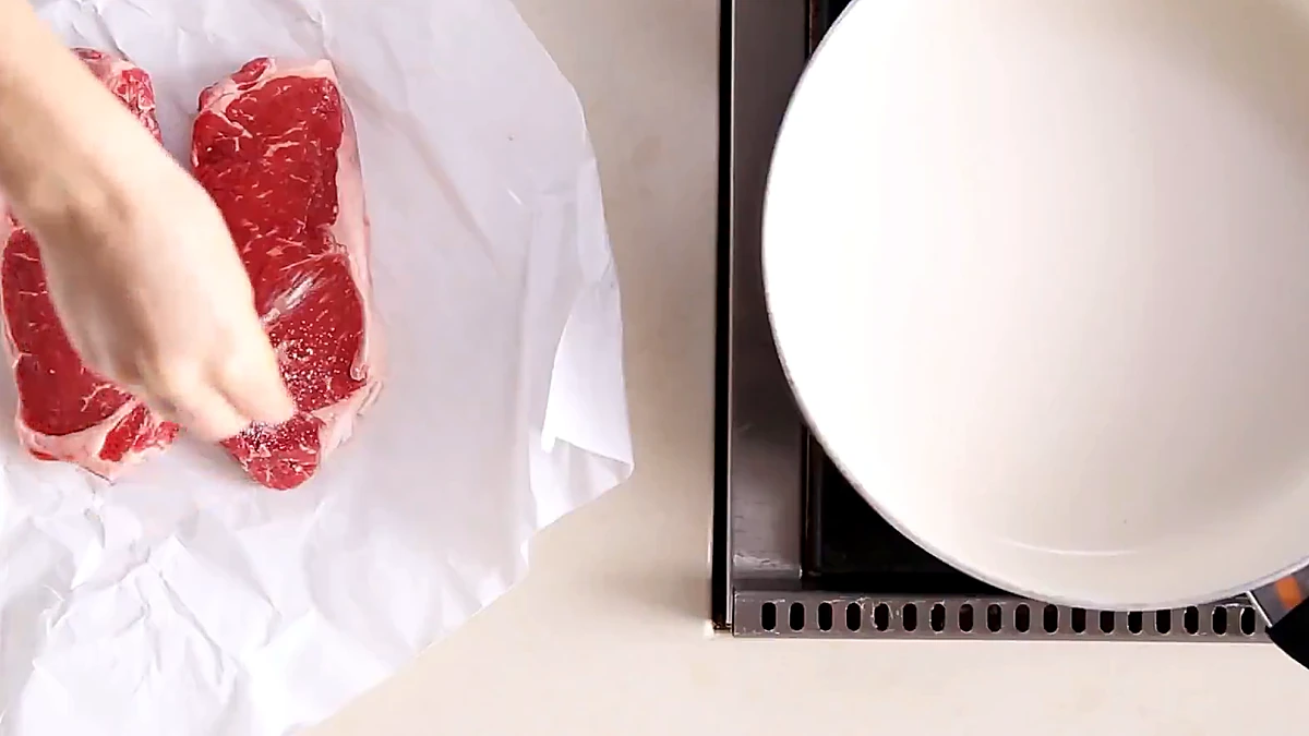 Raw steaks being seasoned with kosher salt on parchment