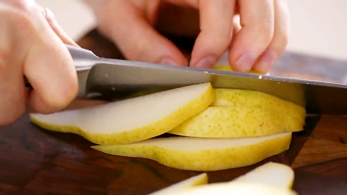 A ripe pear being sliced thin on a cutting board