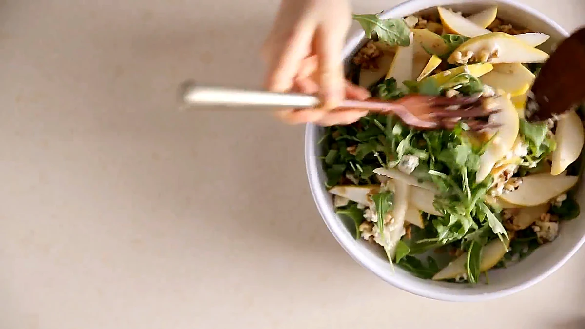 Pear arugula salad being tossed in a white bowl