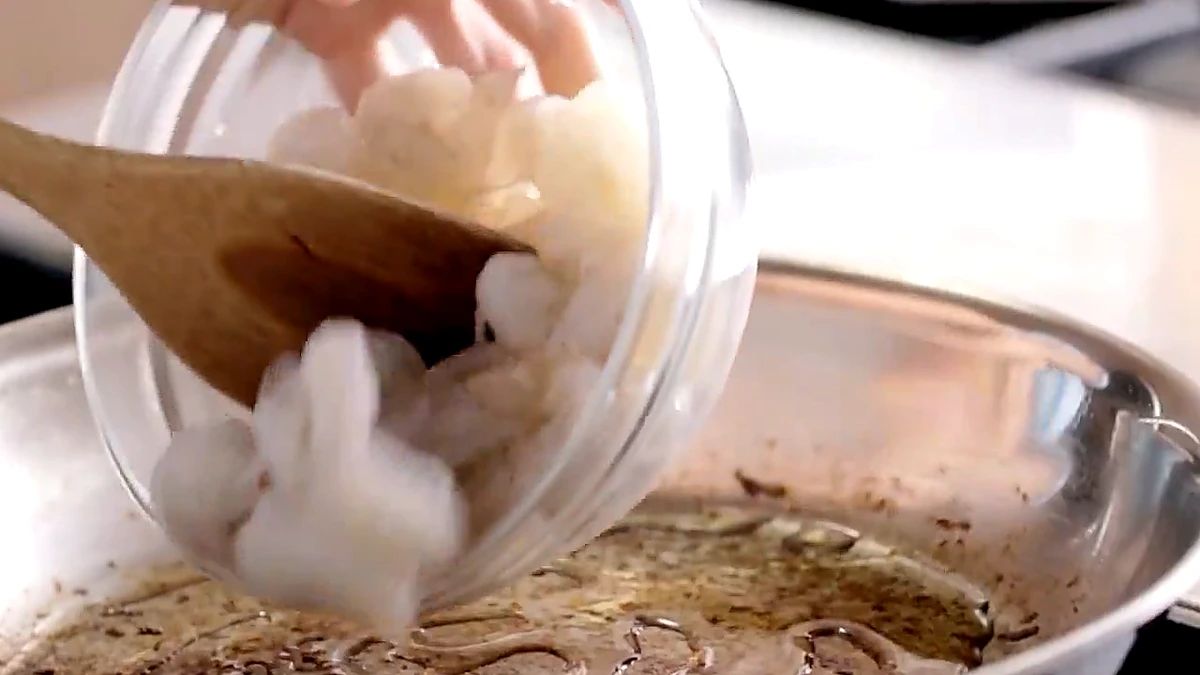 Peeled shrimp being added to a skillet with melted butter