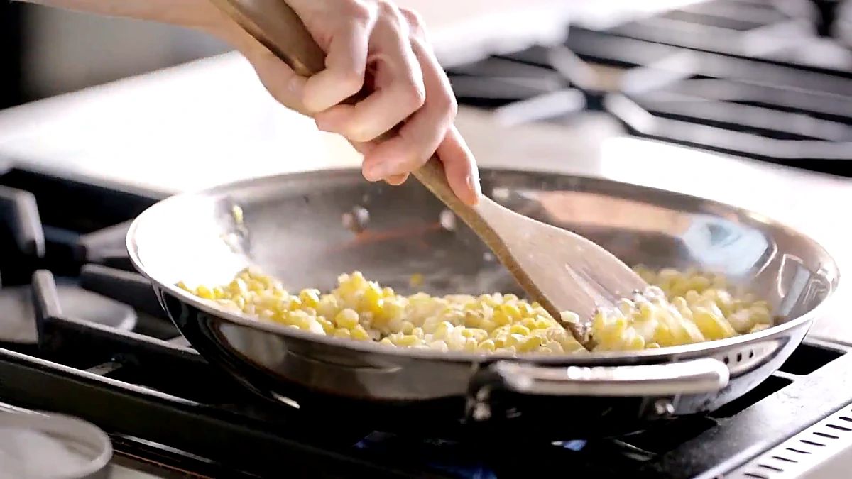 Corn kernels cooking with onion in a stainless skillet