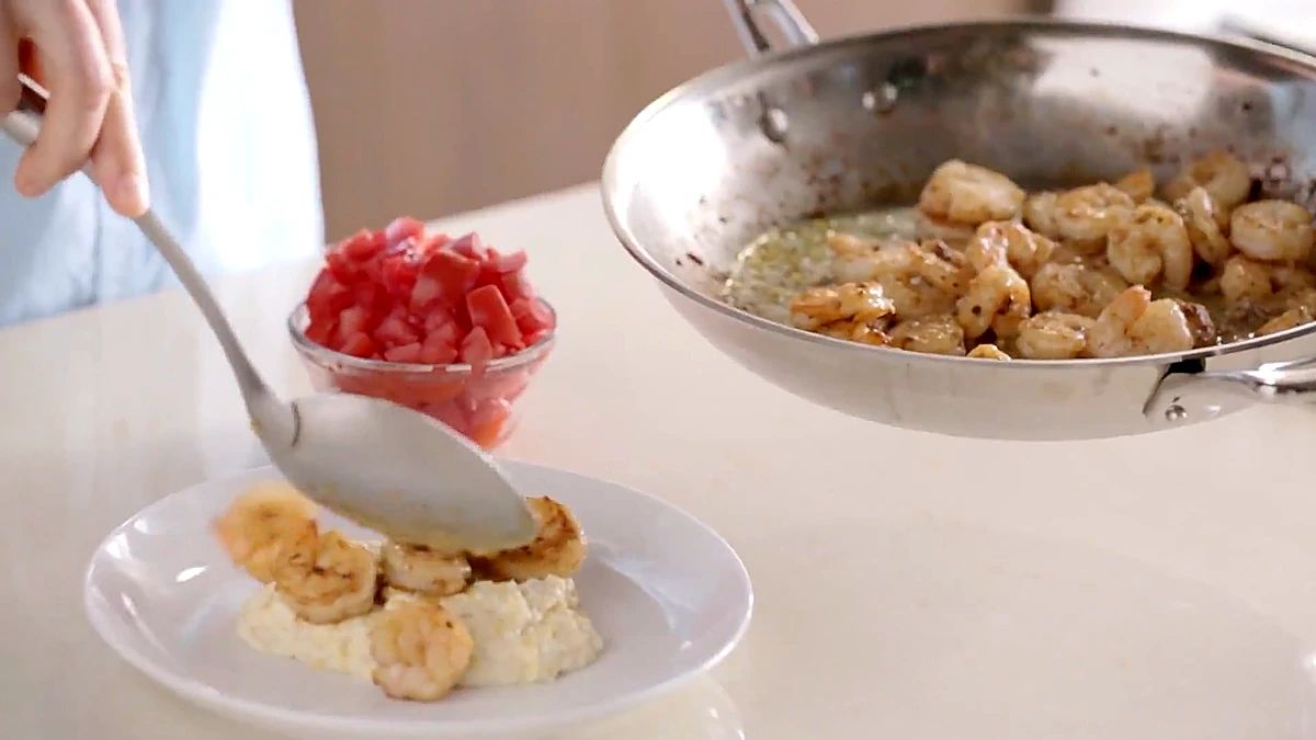 Garlic shrimp and fresh tomato being plated over creamy corn